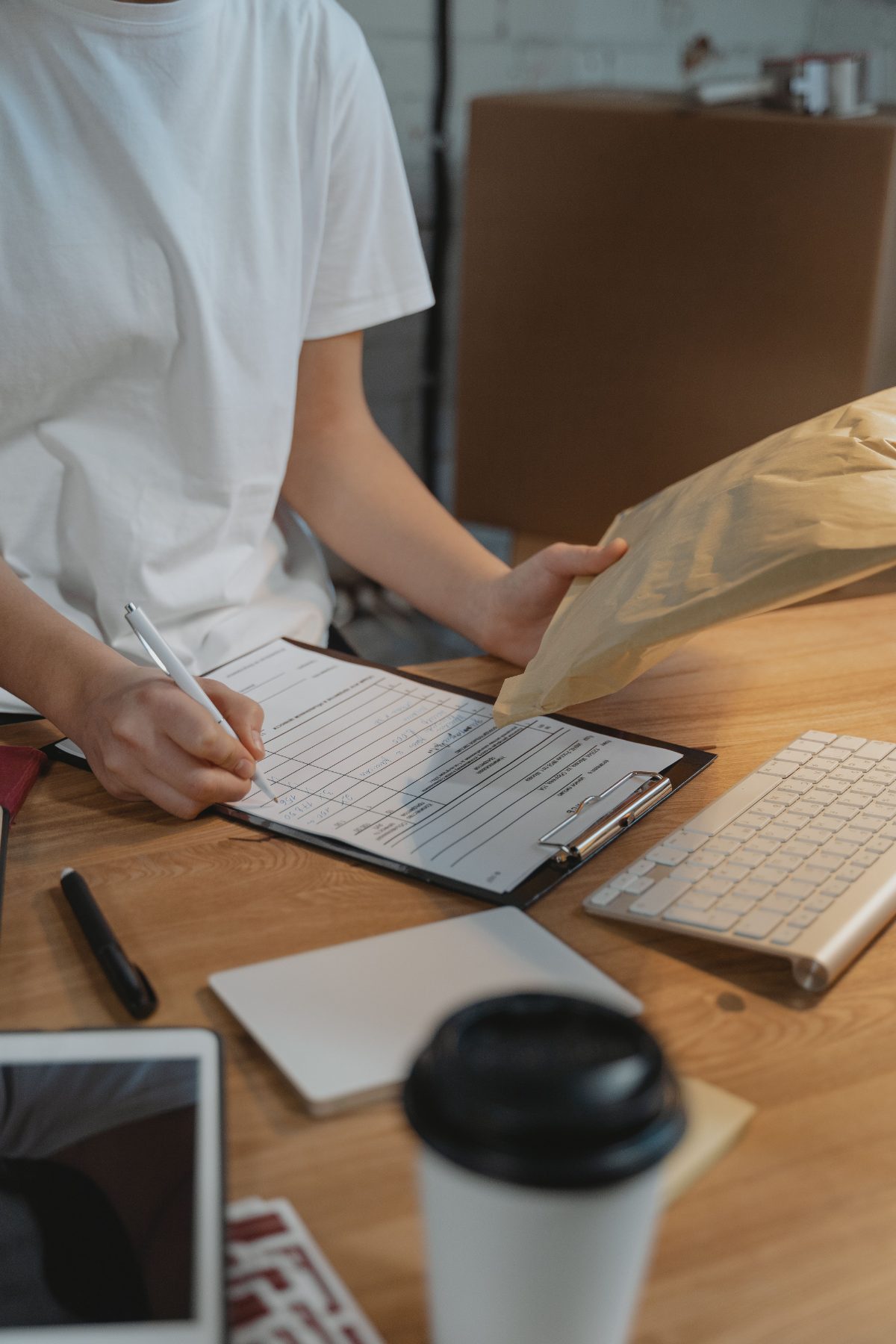 Filling out a shipping manifest on a clipboard beside a kraft mailer